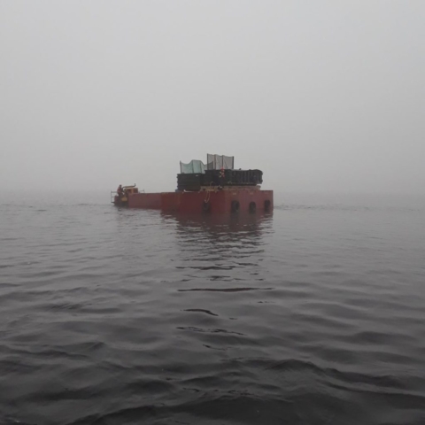 Small barge delivering containment containers to large barges