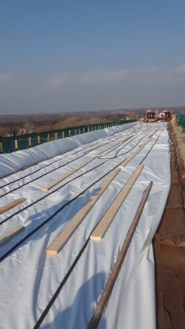 Newly placed deck covered by curing material and tarping, being heated by ground heaters