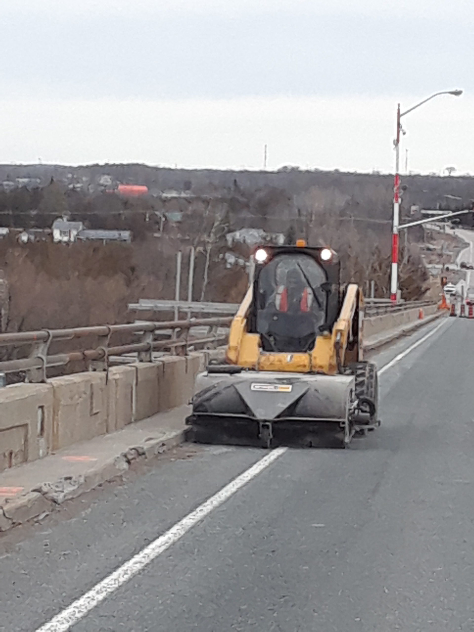 Skid steer with sweeper cleaning the bridge before line painting