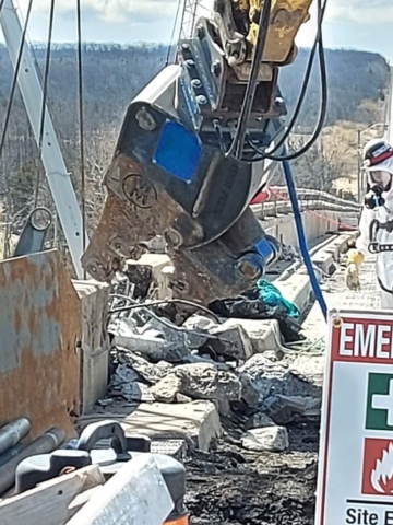 Close-up of barrier wall being removed using an excavator with pulverizing attachment