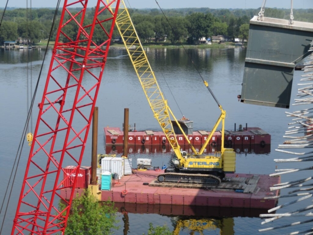 Overview, barge bringing in full containment bin, 200-ton crane holding containment bin