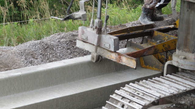 Close-up, slip form machine placing concrete curb and gutter