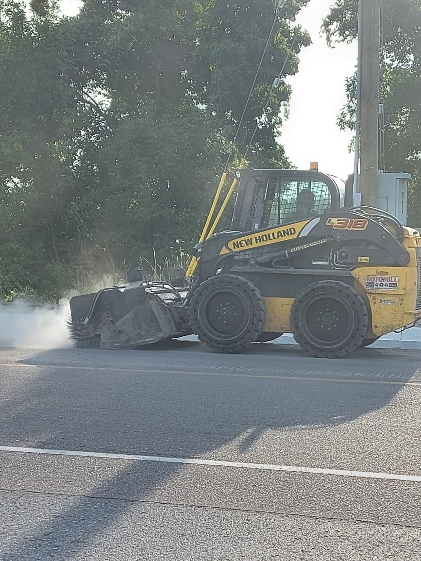 Using the broom attachment to clean the asphalt shoulder